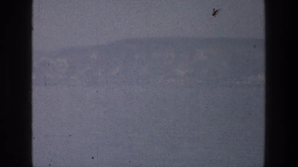 1976 Sea of Galilee home-movie frame showing distant mountains over muted water with visible 8mm scratches and grain.