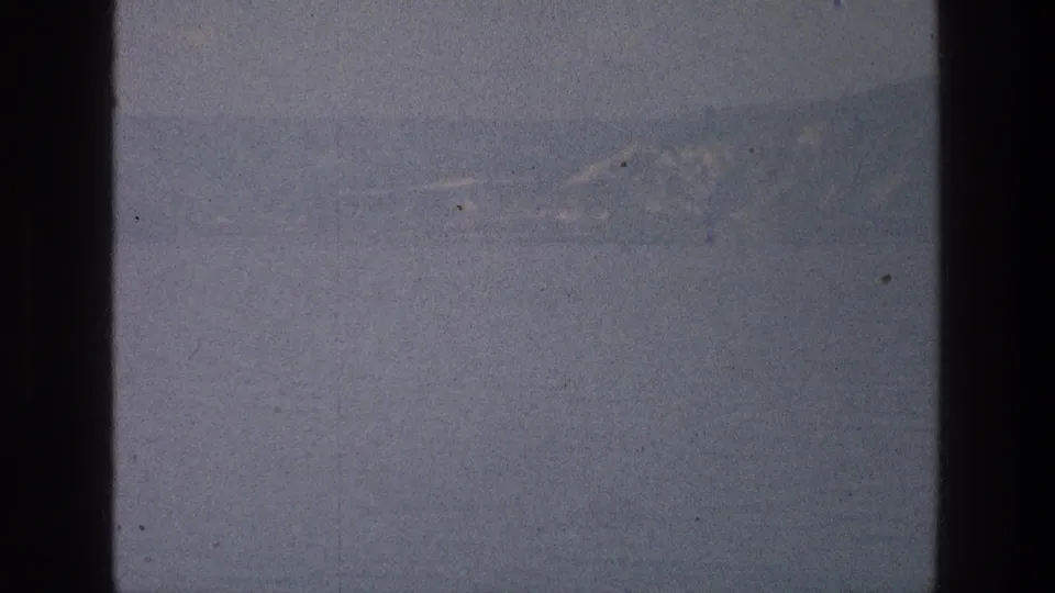 Muted 8mm view of the Sea of Galilee area with far mountains, pale sky, film dust, and dark rounded borders.