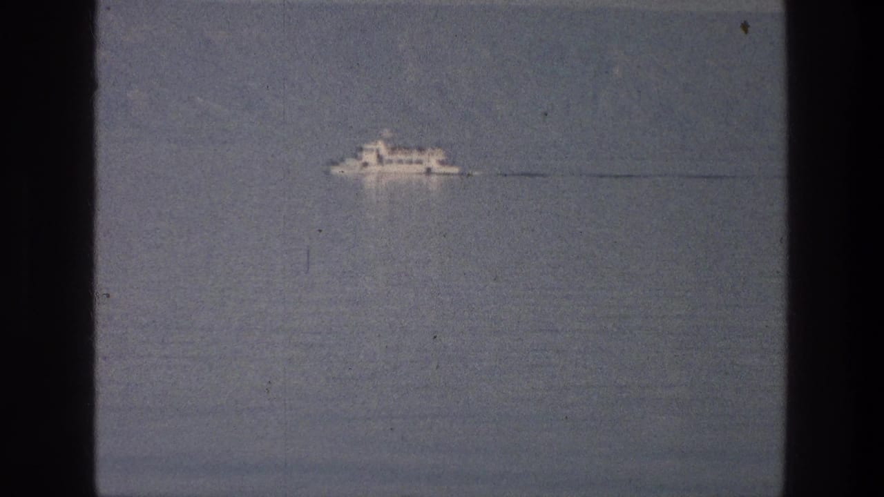 Small white boat crossing calm water beneath a hazy sky.