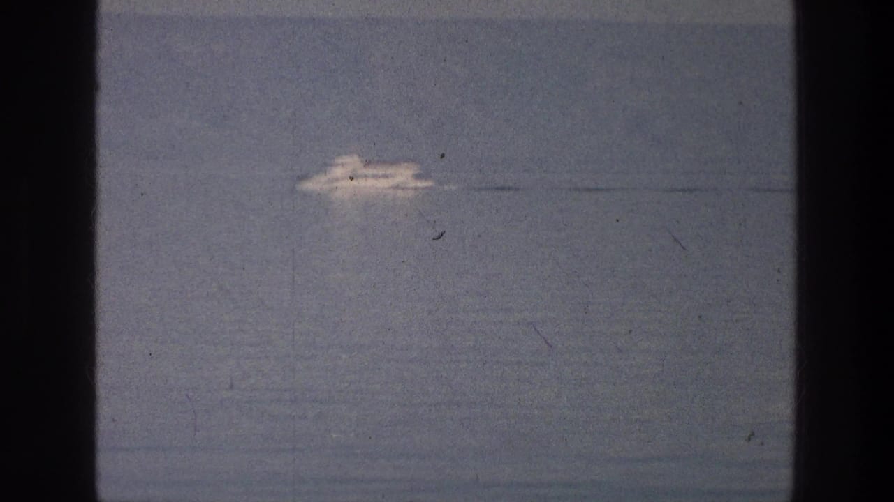 Distant white vessel moving across blue-gray lake water.