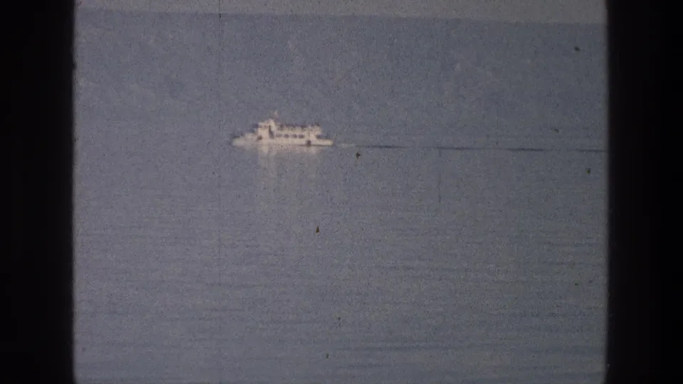 A small white boat is framed low and left on the Sea of Galilee, with subdued water tones and visible 8mm grain.