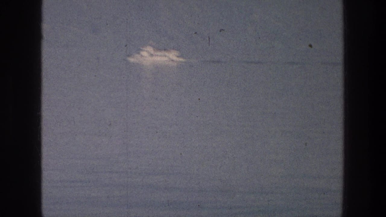 Distant white boat crossing calm water under a muted sky.
