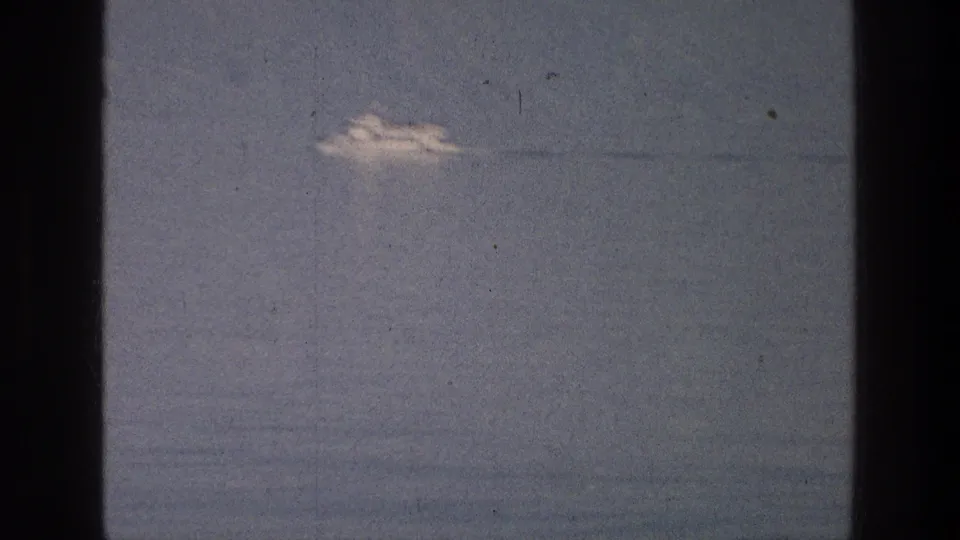 1976 8mm view of a distant white tour boat on the Sea of Galilee, framed by dark film gate edges and visible grain.