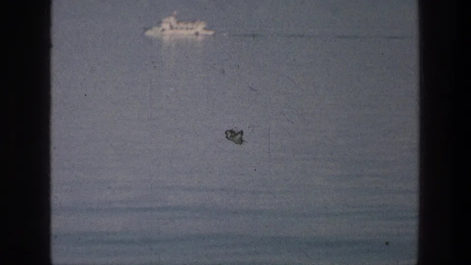 Distant white boat on the Sea of Galilee in a soft 8mm frame with scratches, dust, and blue-gray water.