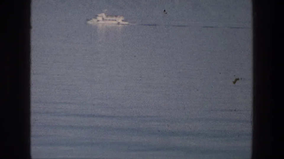 A white multi-deck tour boat crosses the Sea of Galilee in 1976 home-movie footage with grain and gate edges visible.