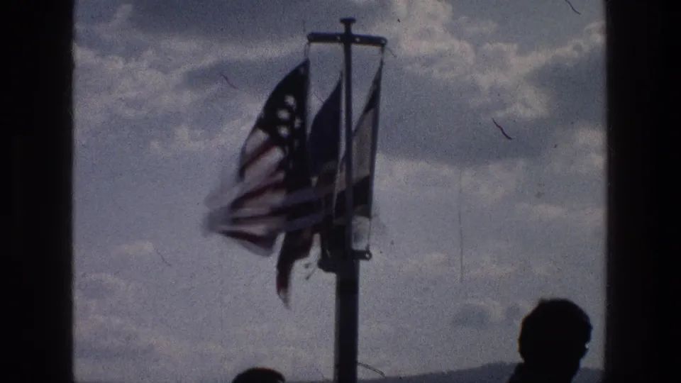 1976 8mm travel footage near the Sea of Galilee shows wind-blurred flags on a pole with dark foreground framing and a low horizon.