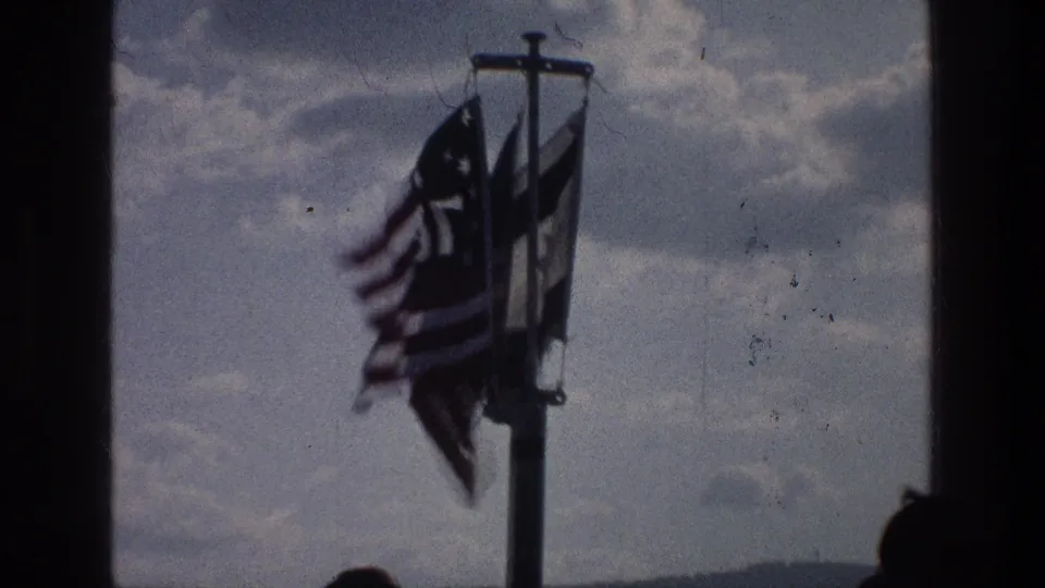 1976 Sea of Galilee boat view with an American flag and another banner fluttering beside a dark window frame.