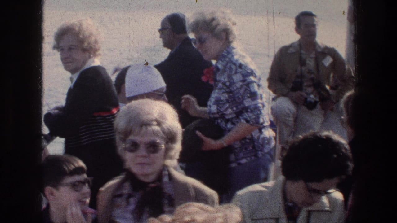 Passengers on a boat deck, including women in sunglasses and patterned clothing, seen beside a dark window bar.