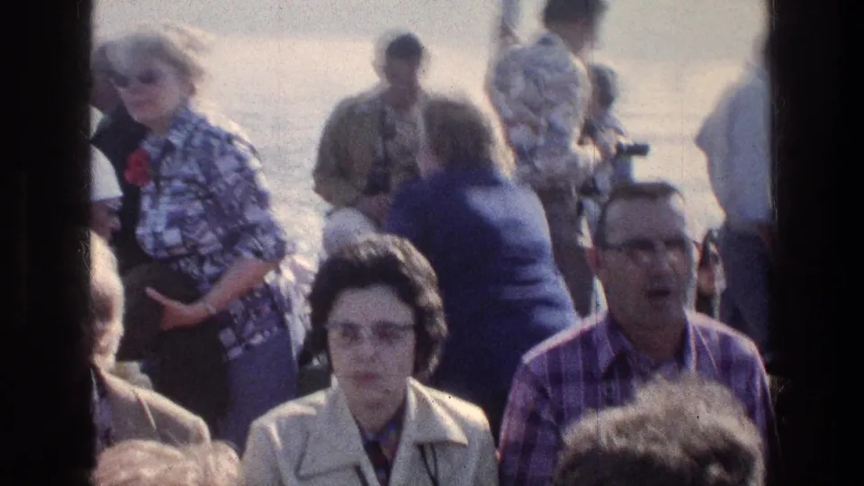1976 Sea of Galilee passengers sit closely on a boat deck, with 1970s glasses and shirts visible through window framing.