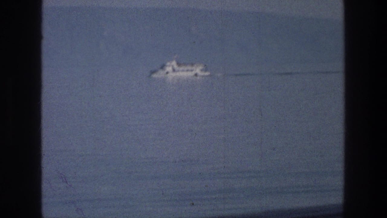Distant white boat crossing calm water with a dark film border at the left edge.