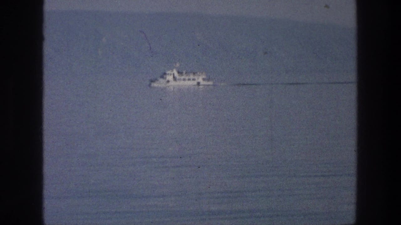 White boat on open water with a long faint wake and dark vertical film borders.