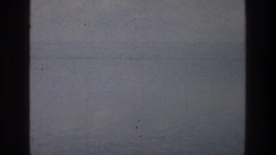 8mm Sea of Galilee frame with misty water, subtle distant landforms, faded color, dust specks, and a dark film border.