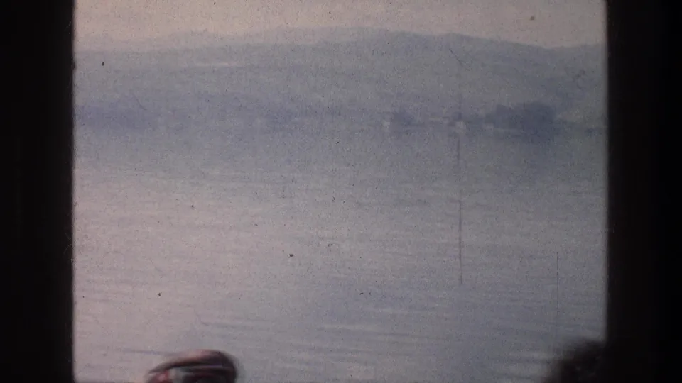 The Sea of Galilee and hazy hills remain framed by dark window dividers, with indistinct passenger heads at the bottom of the frame.