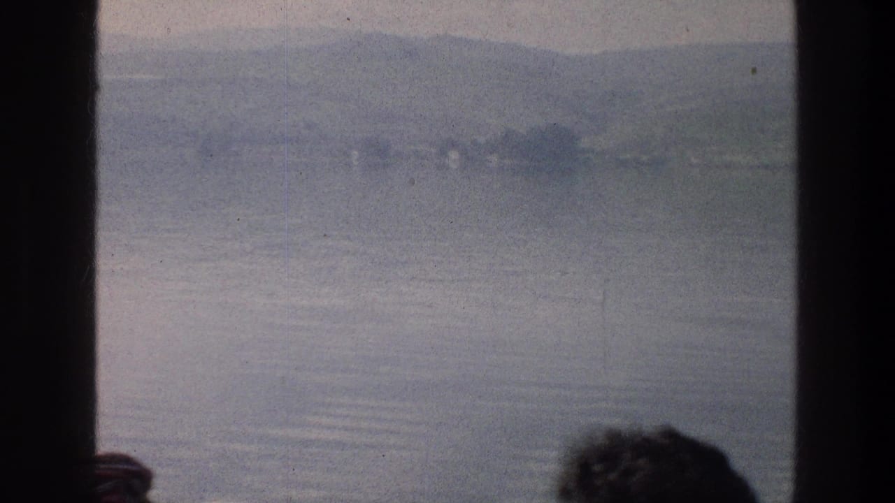 Lake and distant hills seen through dark boat window frames with passenger heads at the bottom.