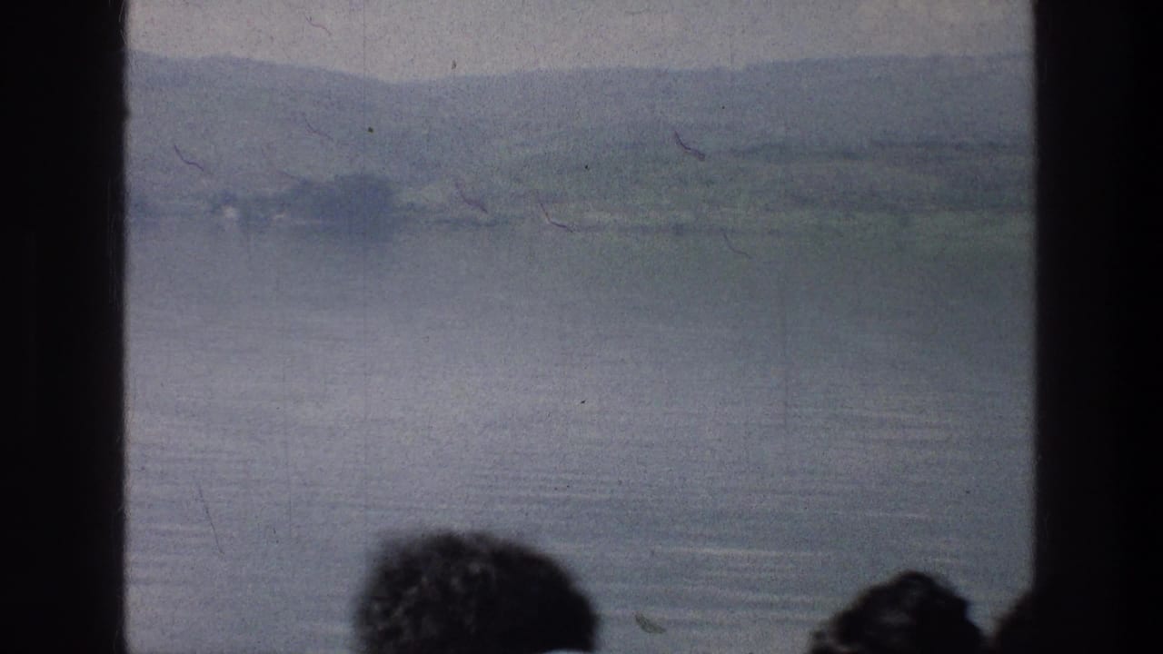 Water and low hills visible through a divided window, with partial passenger heads in the foreground.