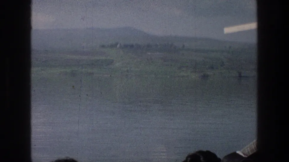 1976 Israel travel footage showing the Sea of Galilee and green hills through a boat window, with a passenger partly visible.