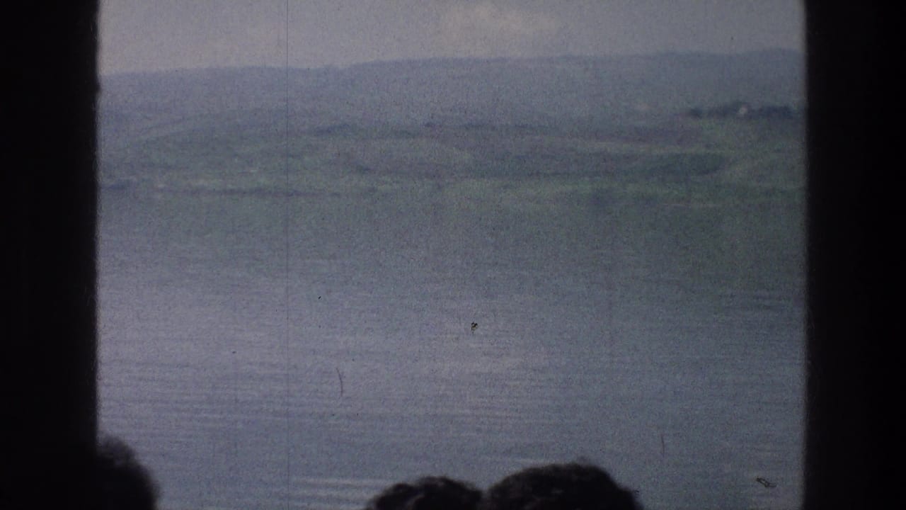 Sea of Galilee landscape in soft 8mm color, seen through a dark central divider with low hills and partial heads near the bottom edge.