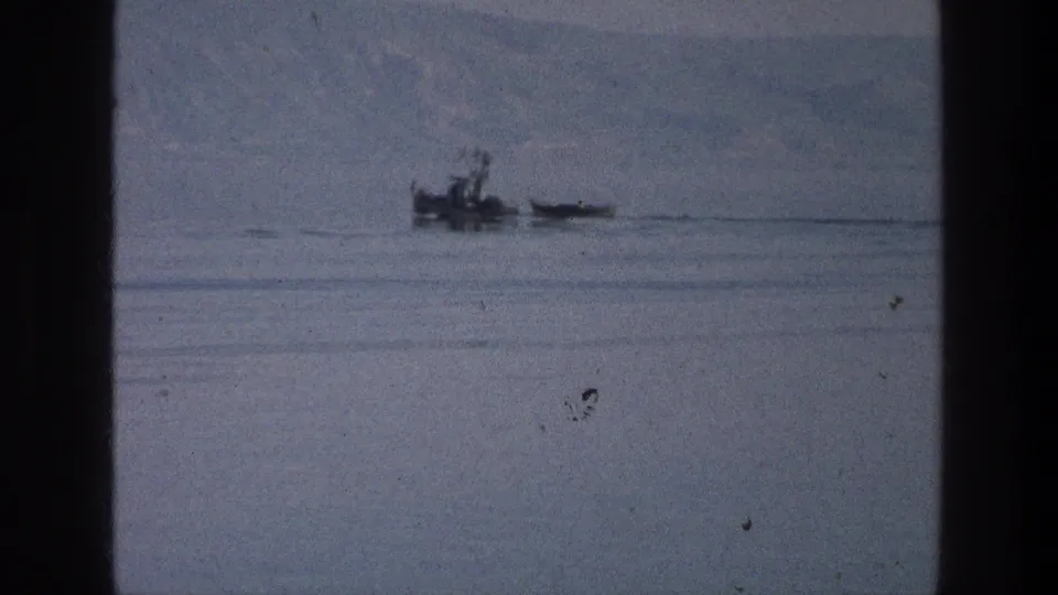 1976 8mm view of a small boat and narrow craft moving across the Sea of Galilee under a hazy sky.