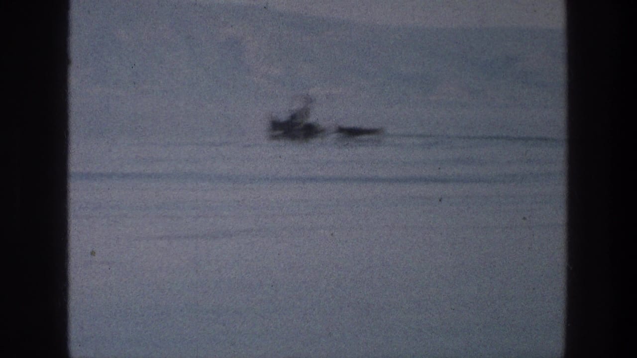 Soft 1976 8mm frame of a small boat and narrow craft on the Sea of Galilee with hills beyond.
