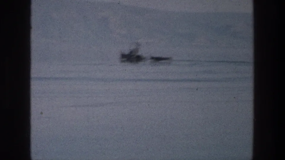 Soft 1976 8mm frame of a small boat and narrow craft on the Sea of Galilee with hills beyond.