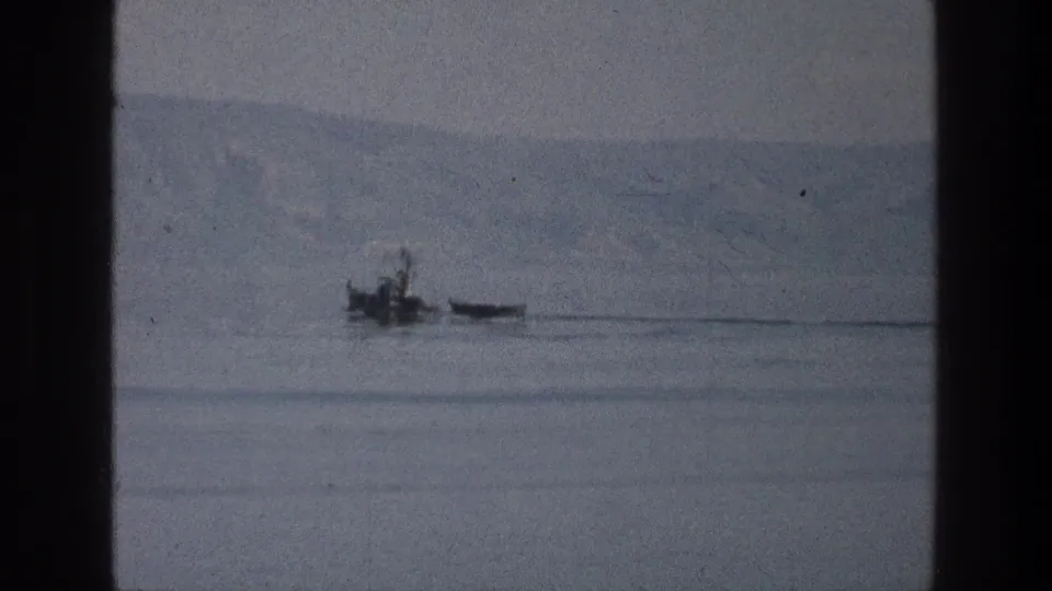 1976 Sea of Galilee home-movie frame showing a small boat beside a narrow craft on still water.