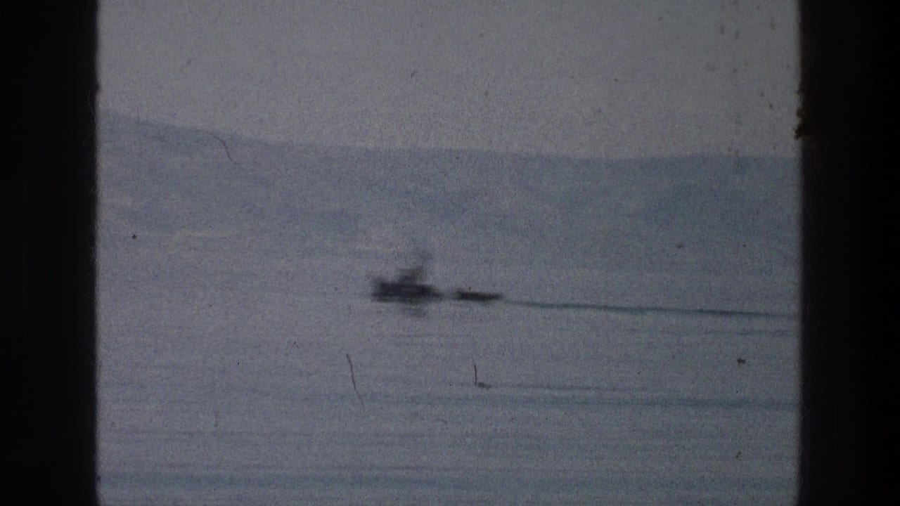 Small boat crossing calm water with distant hills behind dark film gate edges.