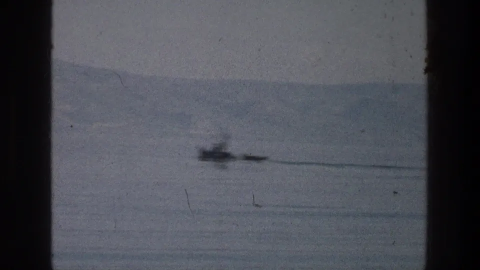 1976 8mm view of a small boat on the Sea of Galilee, with hazy hills and dark film gate borders visible.