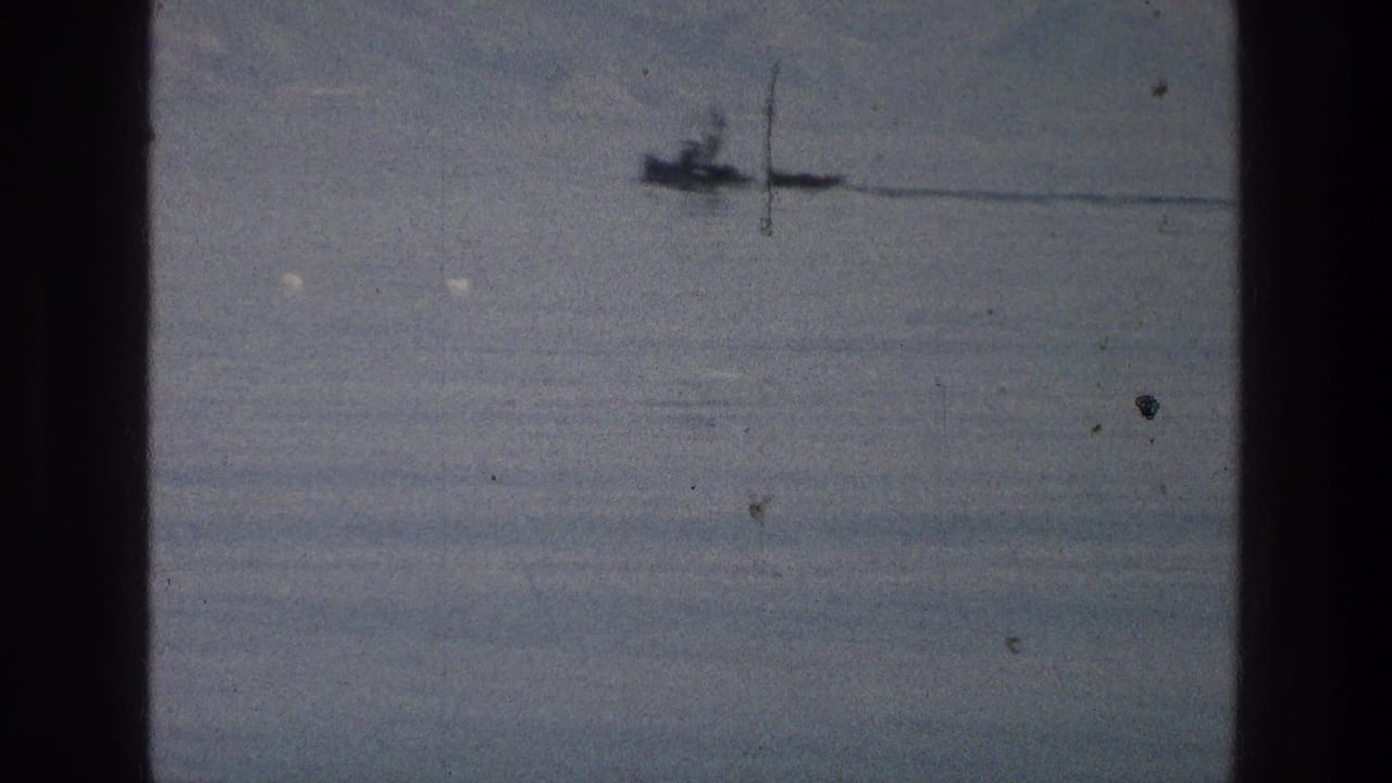 A distant boat crosses the Sea of Galilee in soft 1976 8mm footage, with pale water, haze, and film wear visible.