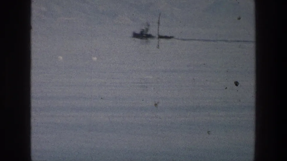 A distant boat crosses the Sea of Galilee in soft 1976 8mm footage, with pale water, haze, and film wear visible.