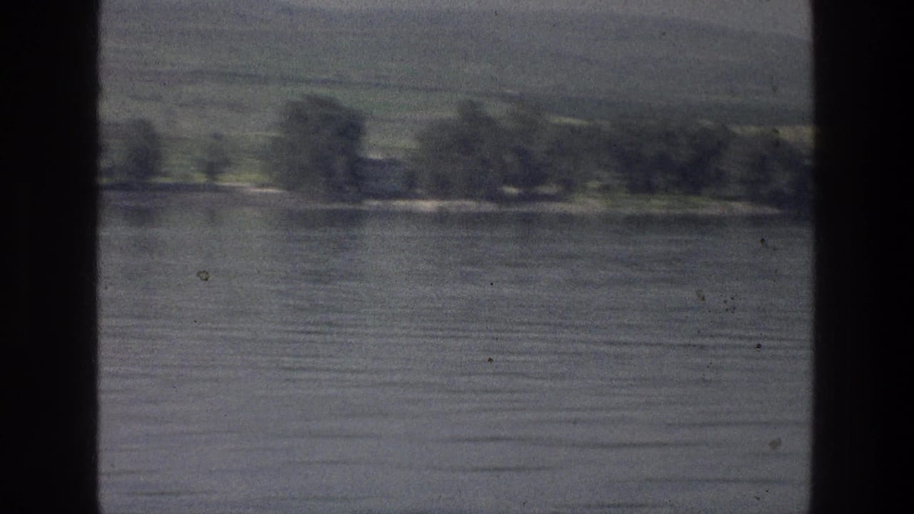 Calm lake water with distant trees and green hills, framed by dark film borders.