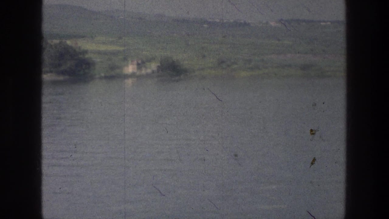 Distant shoreline across lake water, divided by dark boat-window framing.