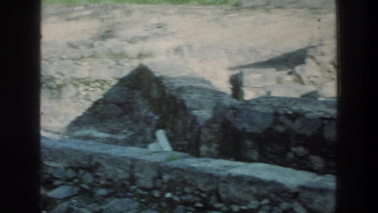 Low stone walls and rocky ground with a small roofed structure at the edge of frame.