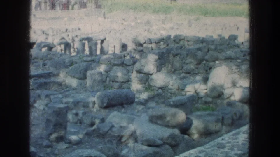 1976 Sea of Galilee ruins with excavated stone rooms, rubble, and distant visitors visible near the top of the frame.