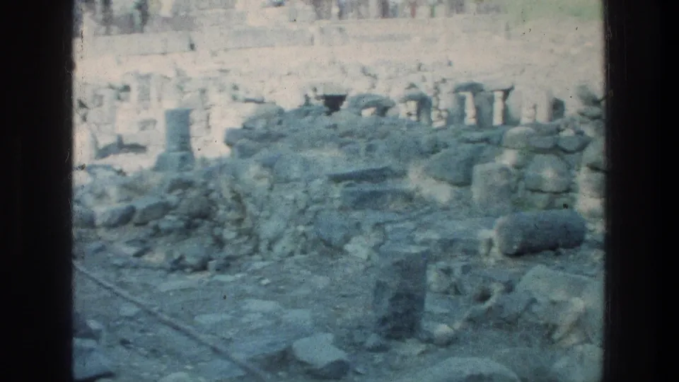 Overexposed 1976 home-movie frame of Sea of Galilee ruins, showing stone paving, fallen blocks, and low wall remains.