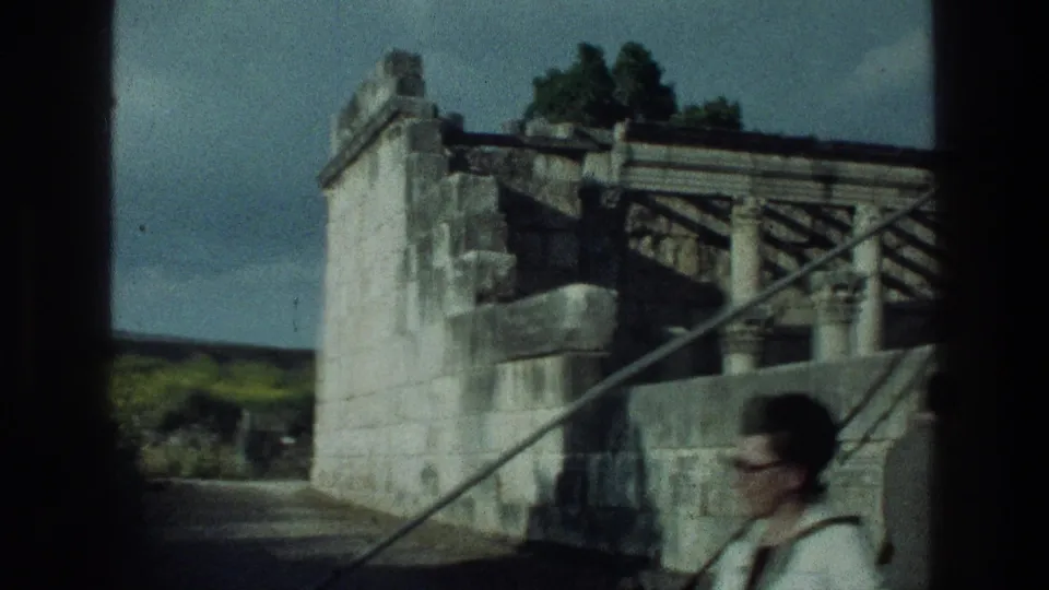 1976 8mm footage near the Sea of Galilee shows a stone structure with railings and a passerby partly visible at lower right.