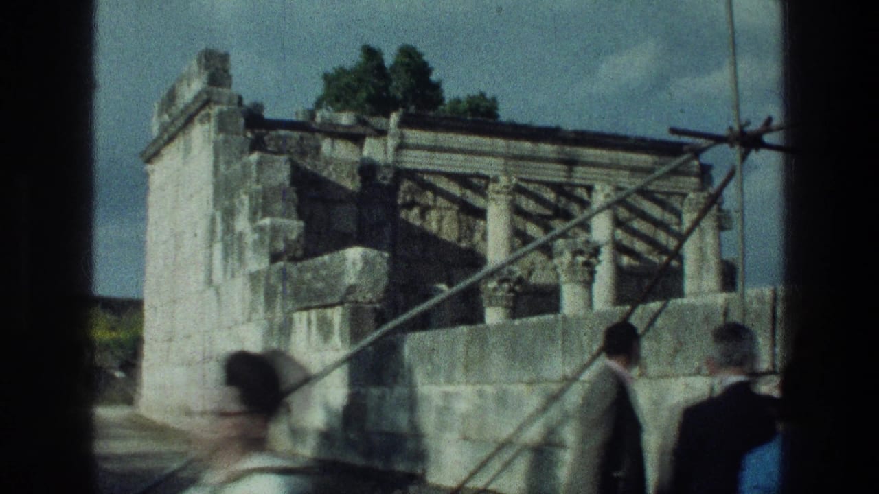 Tourists pass stone ruins with metal supports under bright sun.