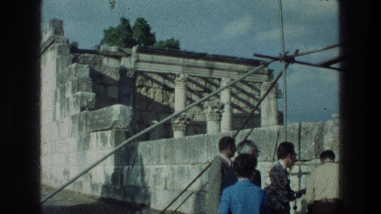 Tourists in 1970s clothing gather by stone ruins near the Sea of Galilee, with columns and metal bracing visible.