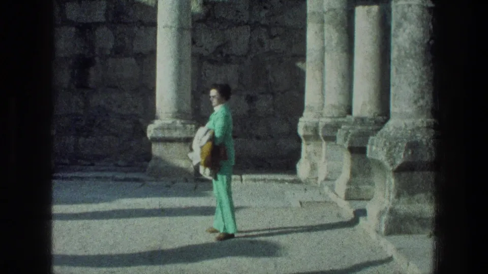 A woman in a green outfit stands near ancient stone columns at the Sea of Galilee ruins in 1976 home-movie footage.