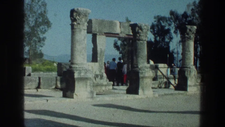 Visitors stand near ancient columns and arch fragments in a 1976 Sea of Galilee travel scene, with trees and hills in the background.