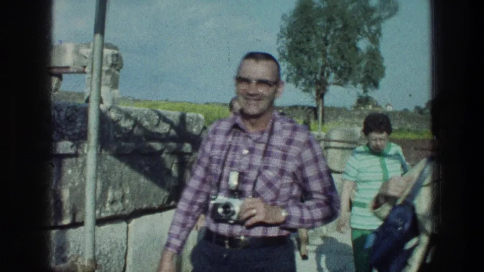 1976 8mm frame showing a man carrying a still camera in an outdoor visitor area near the Sea of Galilee.