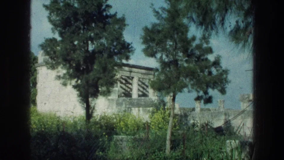 1976 Sea of Galilee home-movie view of a white stone building, trees, hedges, and garden path divided by dark foreground framing.