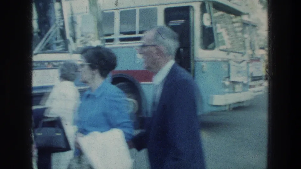 Close street view of pedestrians moving beside a blue and white bus in 1976 Sea of Galilee home-movie footage.