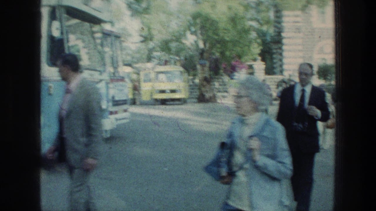Older tourists walk near a blue-and-white bus on a sunlit road.