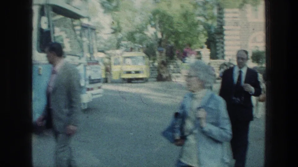 1976 Sea of Galilee travel footage shows older visitors with bags and cameras walking near a bus and roadside buildings.