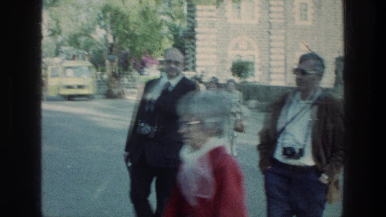 Older visitors carrying film cameras walk along a roadside near stone architecture during a 1976 Sea of Galilee stop.