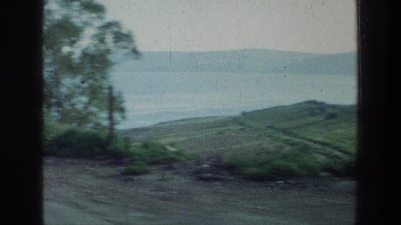 Dirt road and green hillside overlooking hazy lake water with dark film borders.