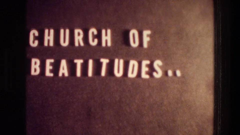 1976 8mm close-up at Tabgha showing a brown Church of Beatitudes sign with white block lettering and dark film borders.