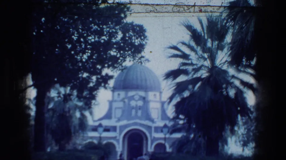 1976 Tabgha church view with a domed facade, arched entrance, palm trees, garden lamps, and shaded foreground foliage.