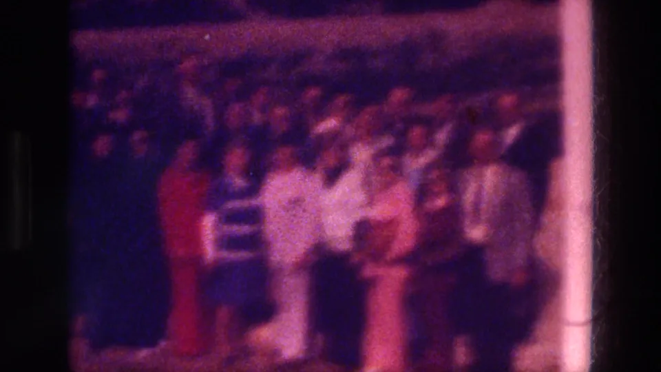 Soft 1976 home-movie frame showing visitors gathered outside the church area, with faces indistinct due to blur and color shift.