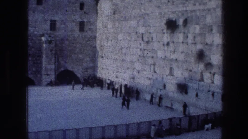 1976 Jerusalem home-movie view of people standing and praying near the Wailing Wall, seen from a distance in blue-tinted 8mm footage.